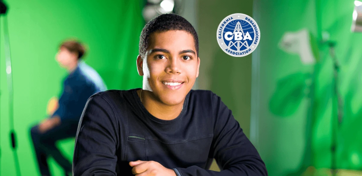 Young man smiling in a green-screen studio; another person blurred in the background. A "California Broadcasters Association" logo is on the wall.